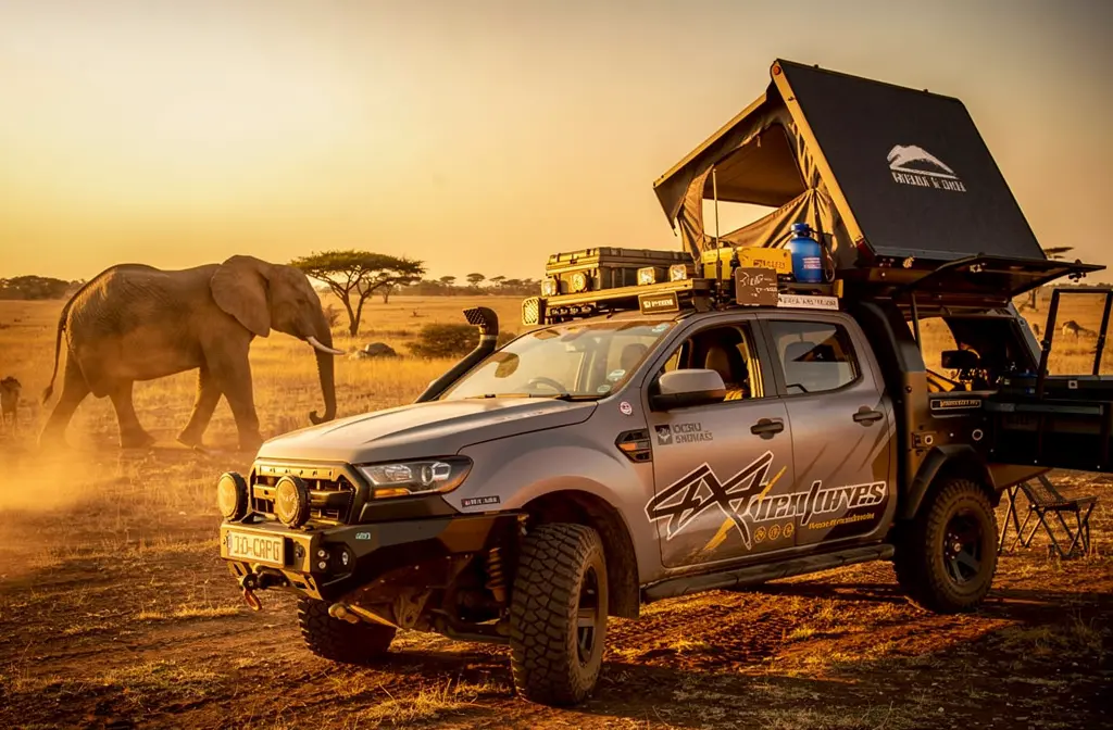 Tente de toit rigide installée sur un 4x4 en pleine savane africaine avec un éléphant en arrière-plan.