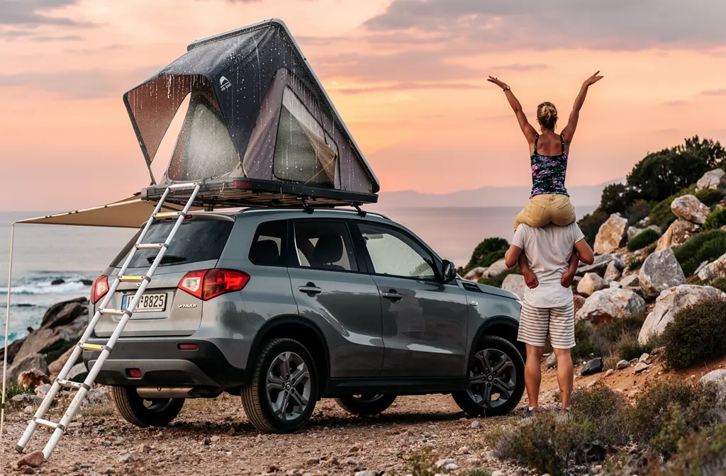 Famille près d’un SUV avec tente toit rigide déployée, rampe et échelle, sur terrain rocheux au coucher de soleil. Concept: tente toit rigide et préparation voyage. Note: tente toit rigide problème condensation est intégré naturellement.